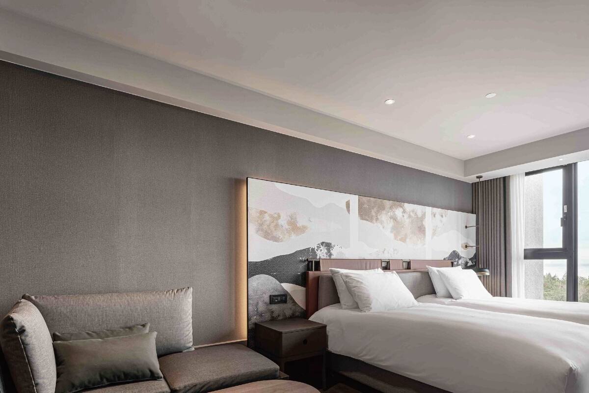 A modern hotel room with a large bed, a seating area, and a view of the outdoors.