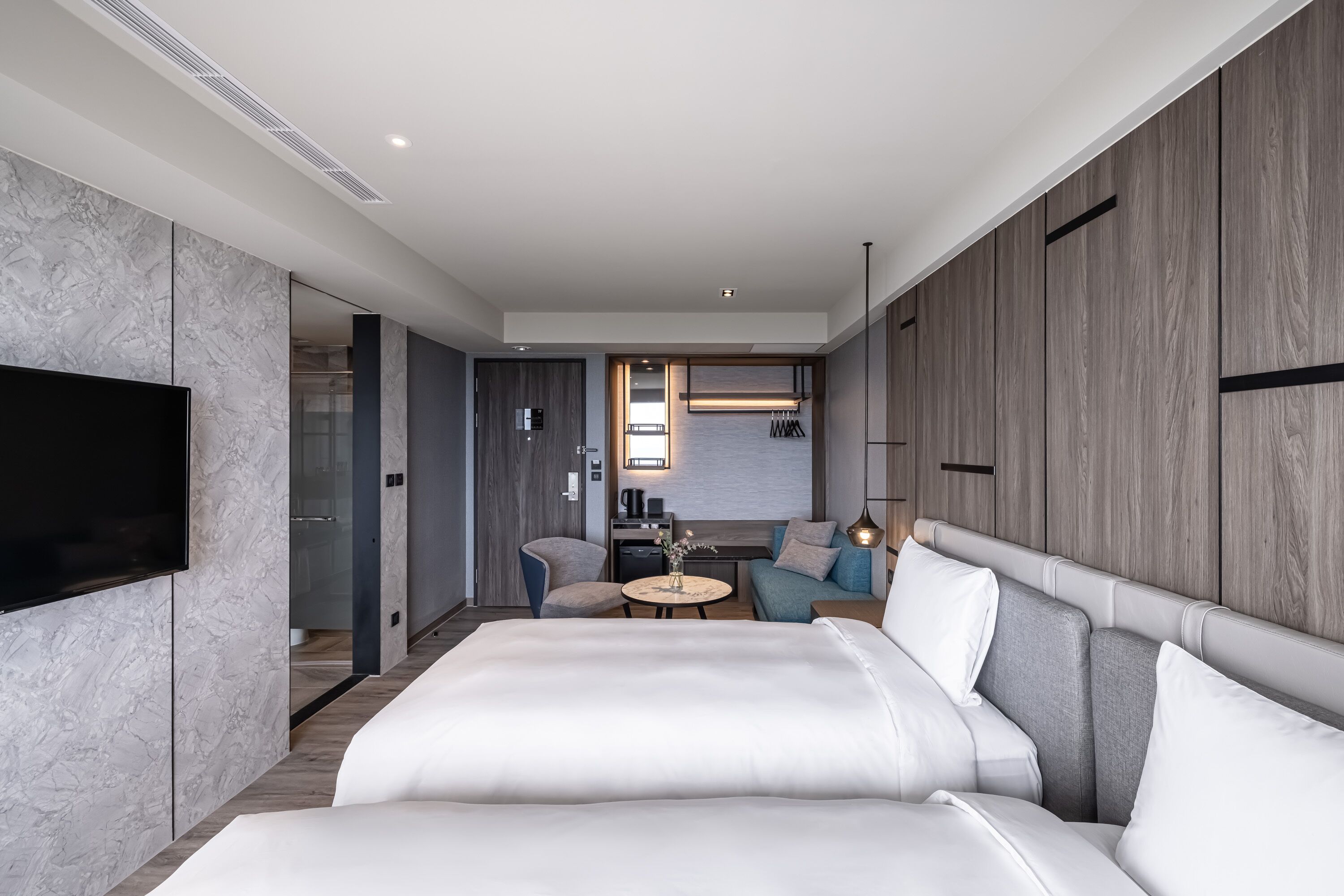 Una habitación de hotel moderna con una cama grande, un televisor, una mesita redonda y una zona de estar con un sofá y sillones.