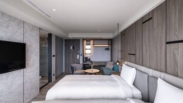 Una habitación de hotel moderna con una cama grande, un televisor, una mesita redonda y una zona de estar con un sofá y sillones.