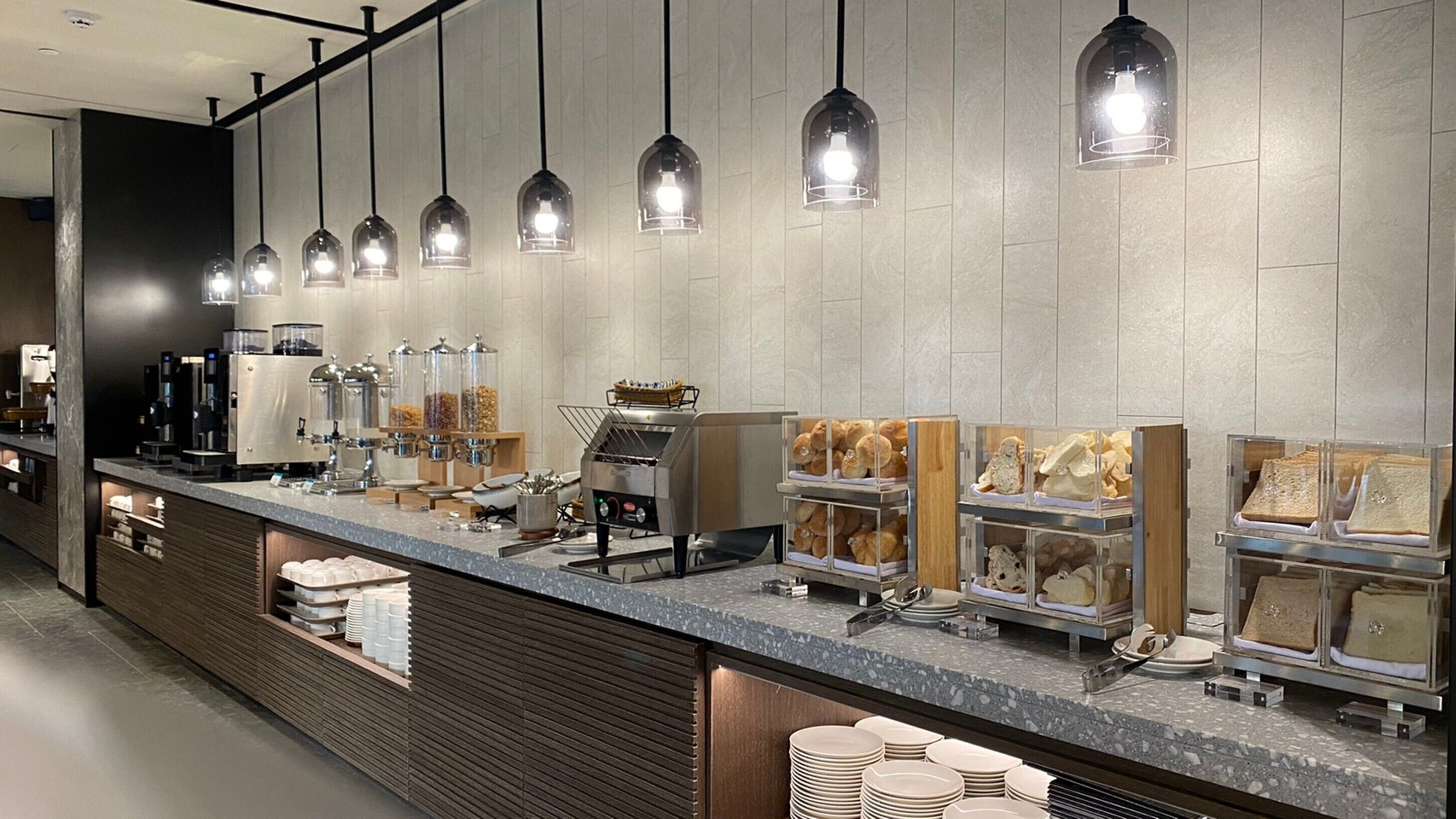 A modern breakfast bar with coffee machines, a bread display, and a coffee dispenser.