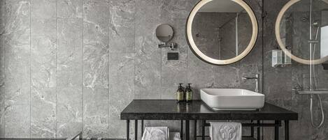 Ein modernes Badezimmer mit Marmorwand, schwarzer Waschtischplatte, weißem Waschbecken, zwei runden Spiegeln und einer Dusche.
