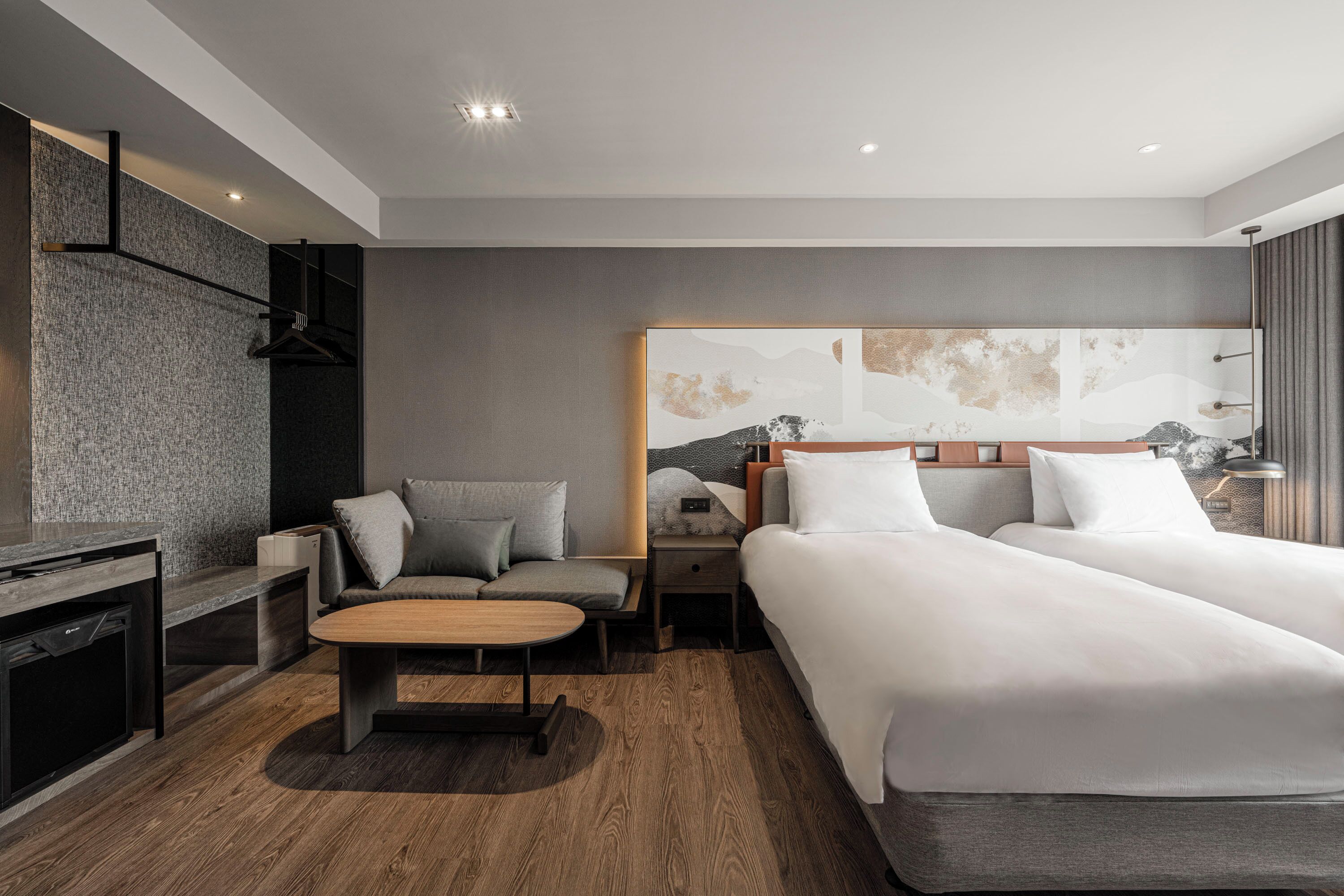 A modern hotel room with two beds, a sofa, a desk, and a large abstract painting on the wall.