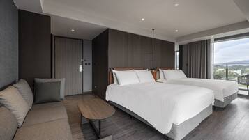 A modern hotel room with two beds, a sofa, a small table, and a large window offering a city view.