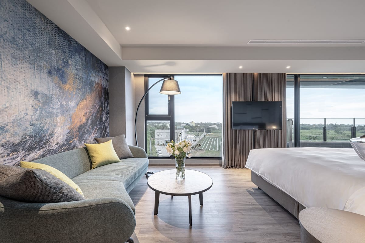 A modern hotel room with a large bed, a sofa, a round coffee table, and a TV.