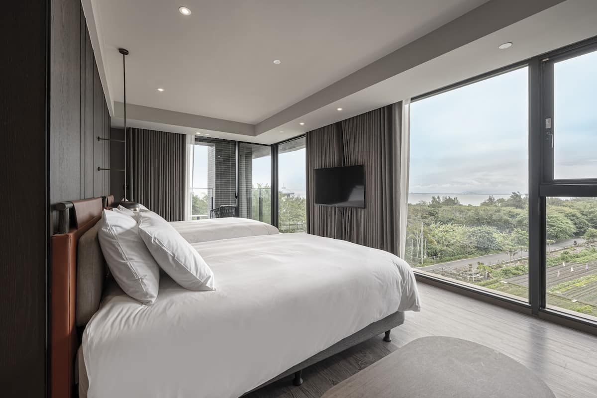 A modern hotel room with a large bed, a flat-screen TV, and a view of the city.