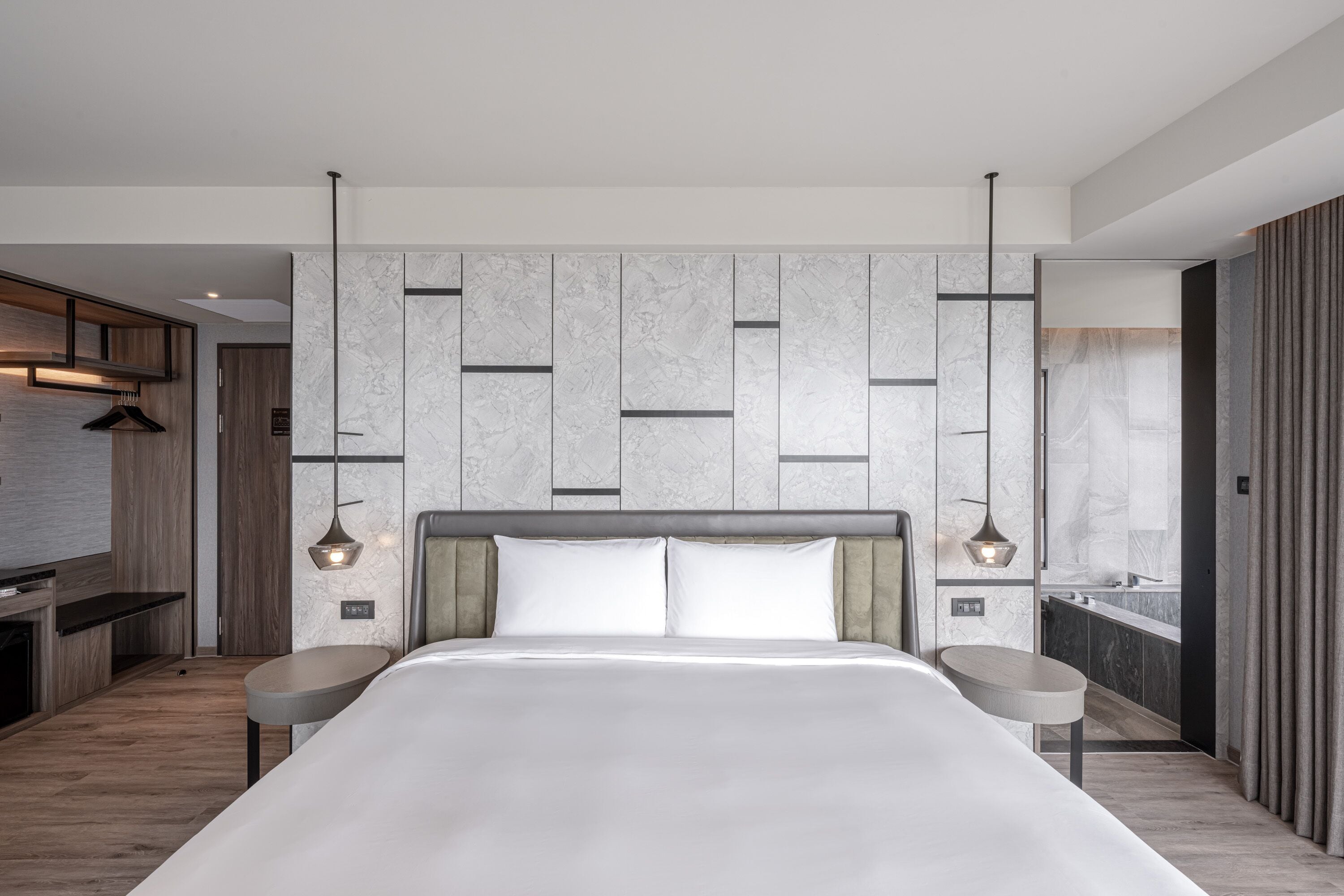 Habitación de hotel moderna con una cama grande, un armario empotrado, una pequeña cocina y un baño con pared de mármol.