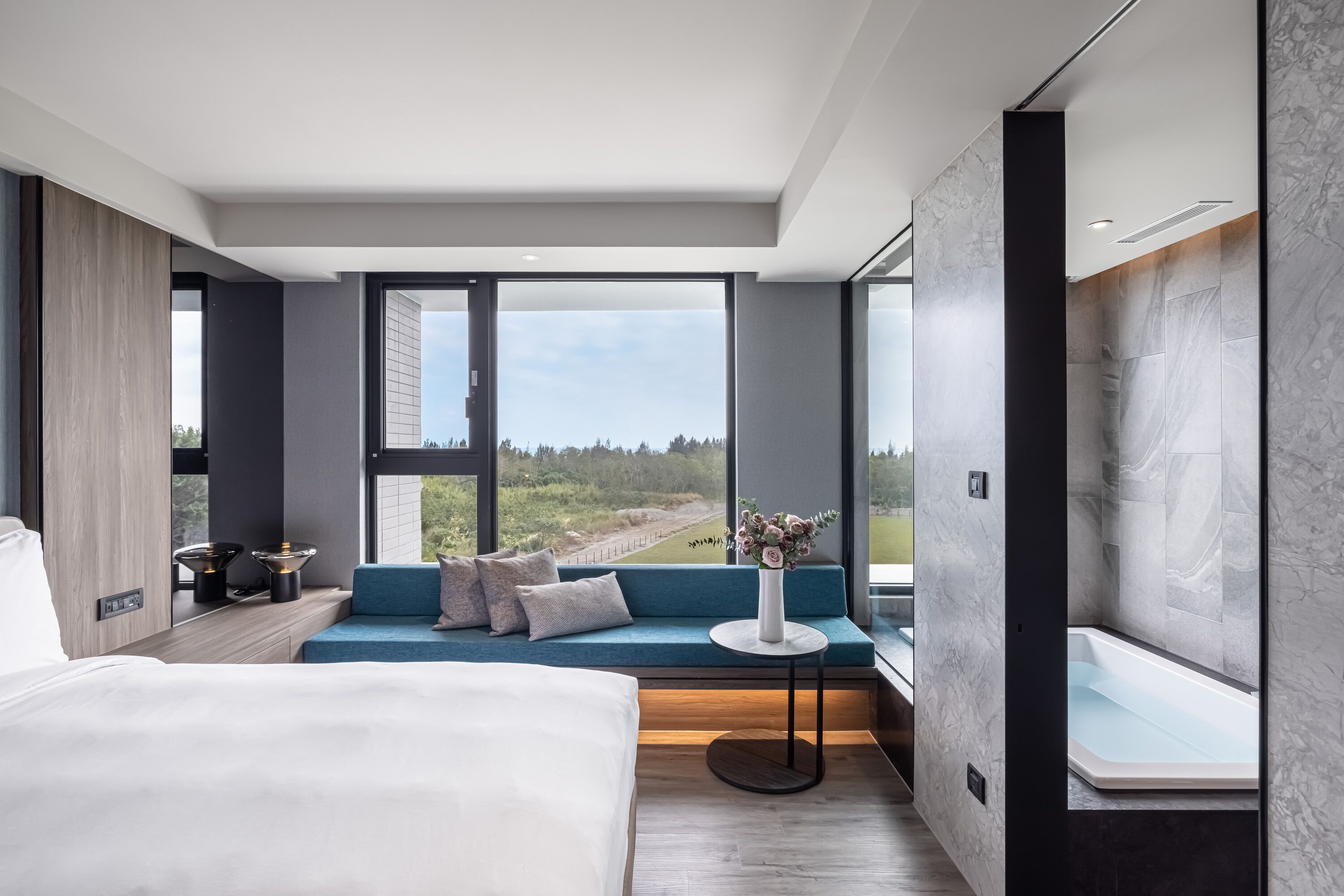 A modern hotel room with a large bed, a seating area with a view, and a bathtub.