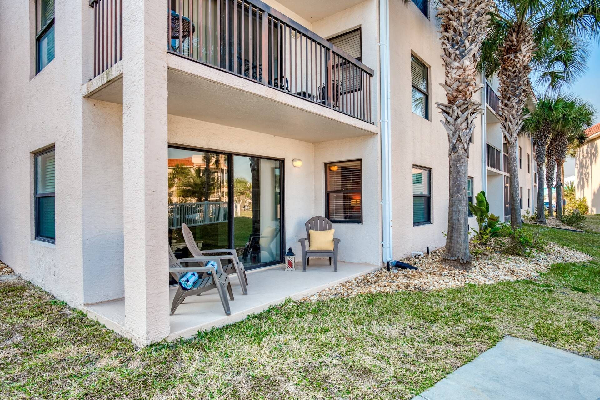 A two-story building with a balcony, outdoor seating, and palm trees.