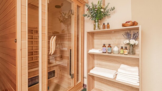 A wooden sauna with glass doors, shelves with towels and essential oils, and a wooden shelf with flowers. - Mržek House with Sauna (Bloke)