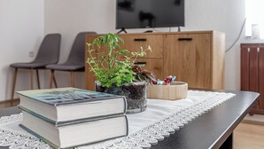 A neatly arranged living area with a television, a wooden cabinet, a potted plant, and a table with books and a lace tablecloth. - Mržek House with Sauna (Bloke)