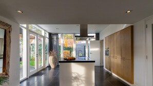 A modern kitchen with a central island, large windows, and a view of the garden. - Luxury holiday home with enclosed garden (Oosterhout)