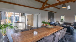 A spacious dining area with a wooden table and grey upholstered chairs, a kitchen with wooden cabinets, and a living area with a sofa and a TV. - Luxury holiday home with enclosed garden (Oosterhout)