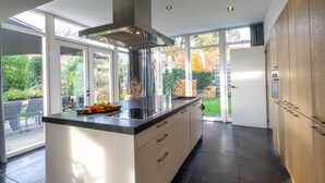 A modern kitchen with a large island, stainless steel appliances, and a view of the garden. - Luxury holiday home with enclosed garden (Oosterhout)