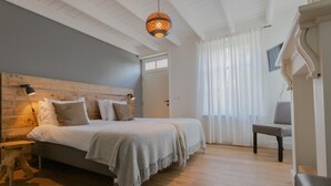 A bedroom with a wooden headboard, a bed with white linens, a grey blanket, a wooden nightstand, a floor lamp, and a hanging light fixture. - Luxury holiday home with enclosed garden (Oosterhout)