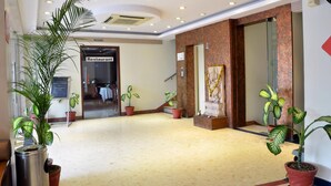 Un hall d’hôtel avec un comptoir d’accueil, une enseigne indiquant l’emplacement du restaurant et des plantes en pot.