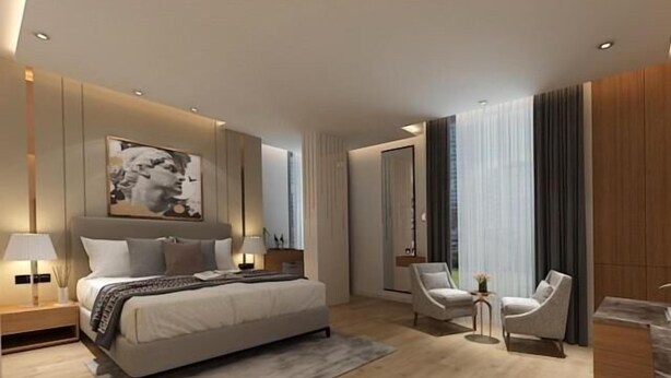 Une chambre d’hôtel moderne, dotée d’un grand lit, de deux fauteuils, d’une petite table d’appoint et d’une grande fenêtre avec des rideaux.