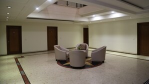 Un hall d’entrée spacieux avec un plafond haut, des luminaires encastrés et un espace salon central comprenant quatre fauteuils.