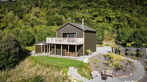 Una casa moderna de dos pisos con balcón, rodeada de exuberante follaje y un jardín bien cuidado.