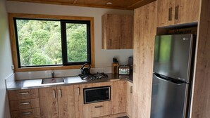 Una cocina moderna con armarios de madera, microondas integrado, refrigerador de acero inoxidable y ventana con vistas a zonas verdes.