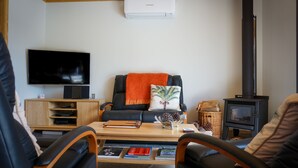 Una sala de estar con un sofá de cuero negro, una mesa de centro de madera, un televisor y un estufa de leña.