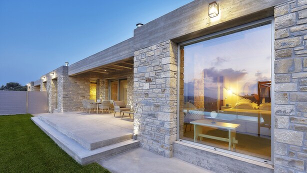 Een modern huis met stenen buitenmuren, grote glasramen en een terras met tuinmeubilair.