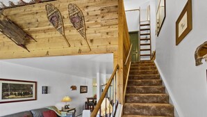 Eine Treppe mit Holzwertlauf, die zu einer oberen Etage führt, mit braunem Teppich, einer Holzzielung mit Verzierungen, einem Ledersofa mit roten Kissen und einem gerahmten Bild an der Wand.