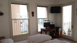 A bedroom with two beds, a desk with a computer, a TV on the wall, and large windows with a view of the outside. - Exclusive duplex near Jaffa fishermen port and old city, Family (Tel Aviv)