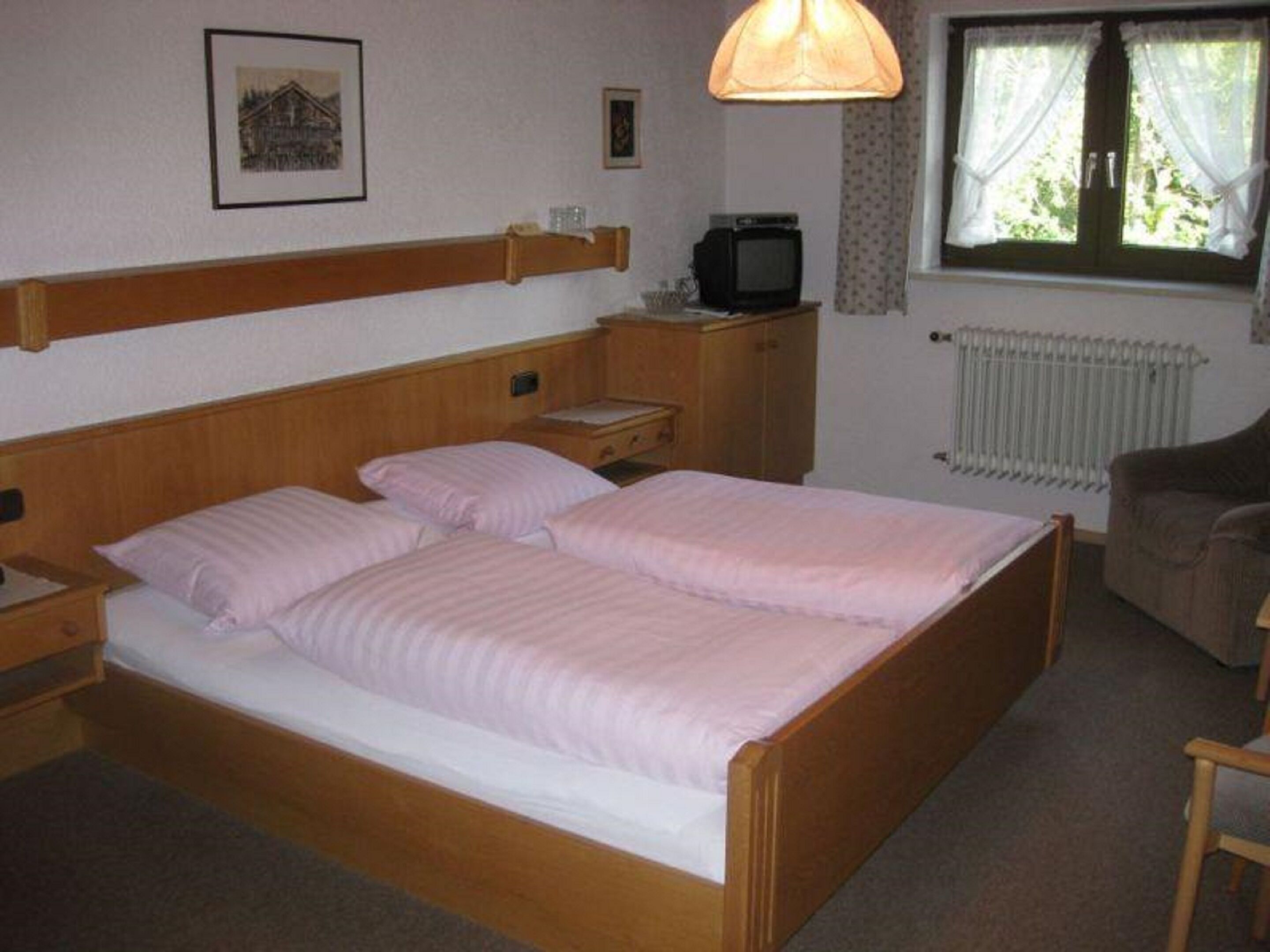 Un dormitorio con una cama de madera, una mesita de noche, un televisor y una ventana con cortinas.