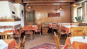 A restaurant with wooden paneling, tables with orange tablecloths, and hanging pendant lights. - Pension & Fewos Fuchs (Mauth)