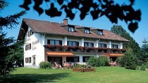 A large, two-story building with a sloped roof, multiple balconies, and a well-maintained lawn. - Pension & Fewos Fuchs (Mauth)