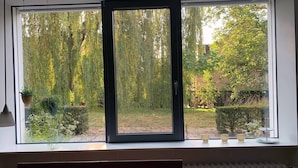 A room with a large window overlooking a garden with various plants and trees. - F80-Die FEINE Ferienwohnung (Regensburg)