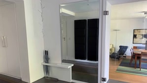 A modern interior with a sliding door leading to a dark room, a white cabinet with a shelf, and a dining area with a table and chairs. - F80-Die FEINE Ferienwohnung (Regensburg)