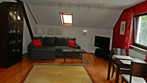 Una sala de estar con un sofá seccional, una mesita, un televisor y una ventana con cortinas.