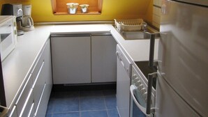 Cocina compacta con ventana, armarios blancos, refrigerador y cafetera.