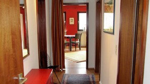 Un pasillo con un aparador rojo, una alfombra estampada y un comedor al fondo.