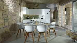 Una cocina moderna con armarios blancos, una pared de piedra y un comedor con sillas blancas y una mesa de madera.