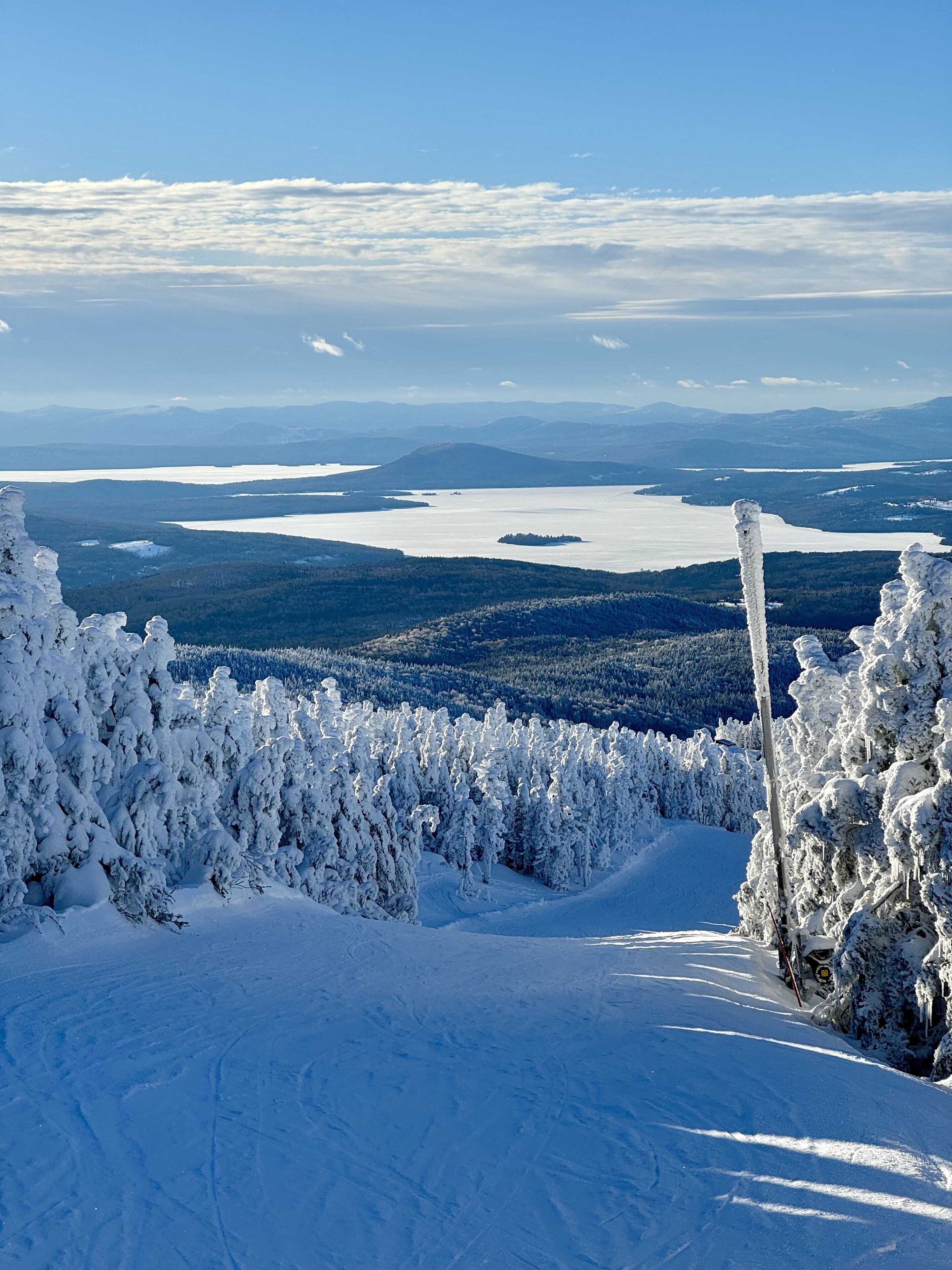 Un paysage enneigé offrant une vue dégagée sur un lac et des montagnes lointaines.