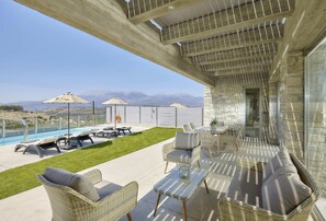 A covered outdoor patio with wicker furniture, a pool, and a view of mountains.