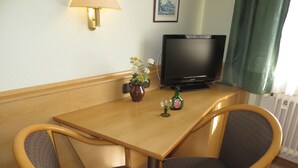 A hotel room with a wooden table, two armchairs, a television, a vase with flowers, and a bottle of liquor. - Rotes Ross Burghaslach (Burghaslach)