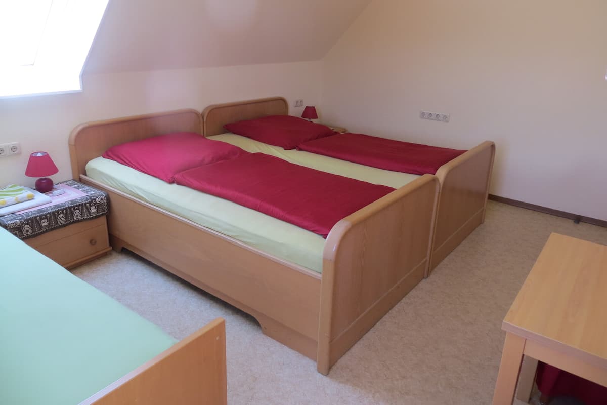 A single bed with a wooden frame, a bedside table with a lamp, and a small desk in a room with a sloped ceiling.