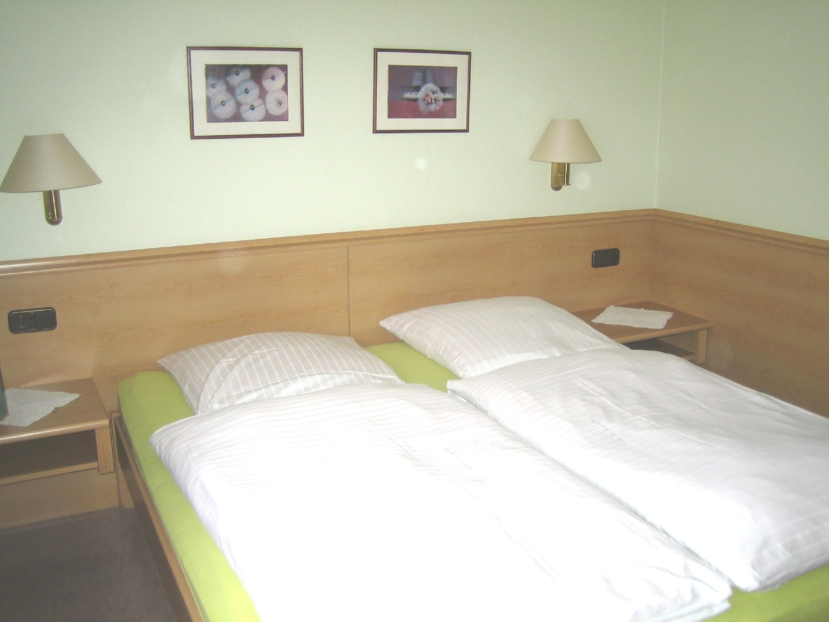 Ein Hotelzimmer mit einem Doppelbett, zwei Nachttischen, zwei Wandleuchten und zwei gerahmten Bildern an der Wand.