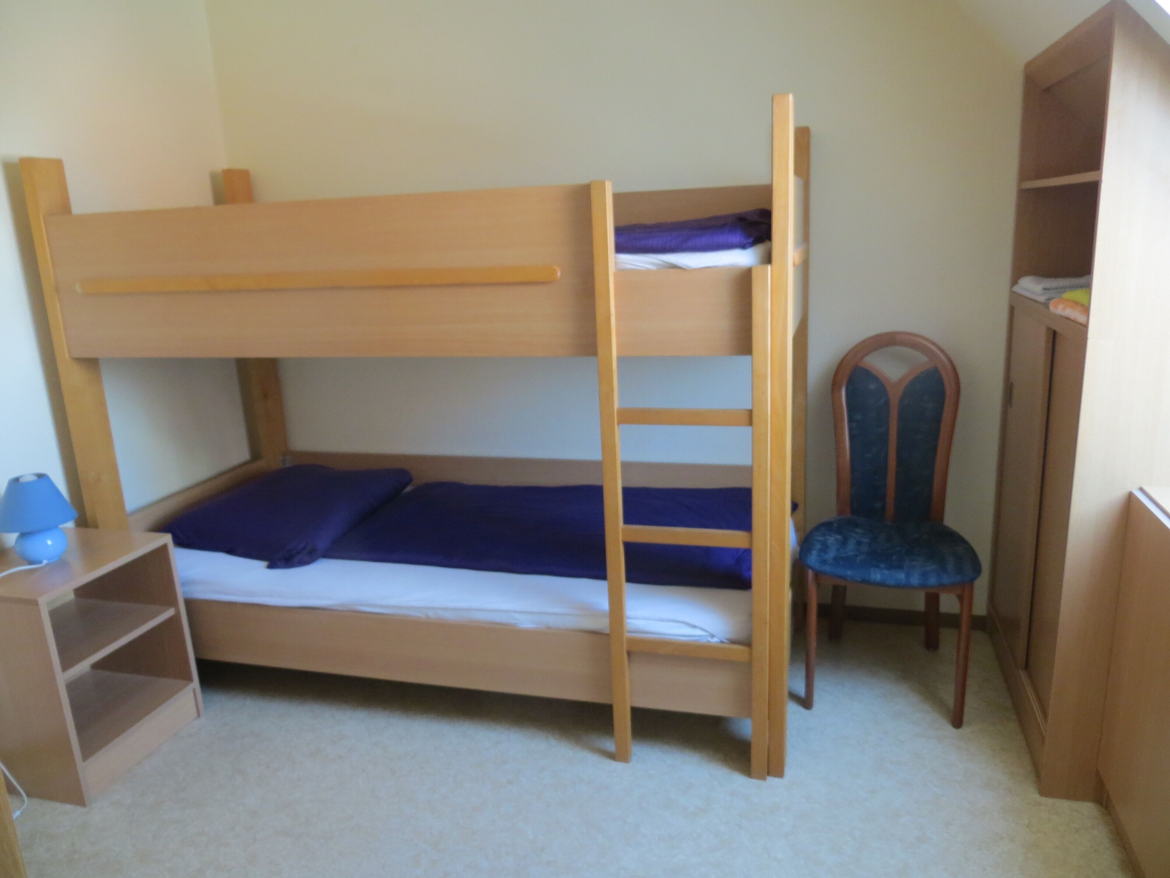Un lit superposé avec une échelle, une chaise et un petit bureau avec une lampe.