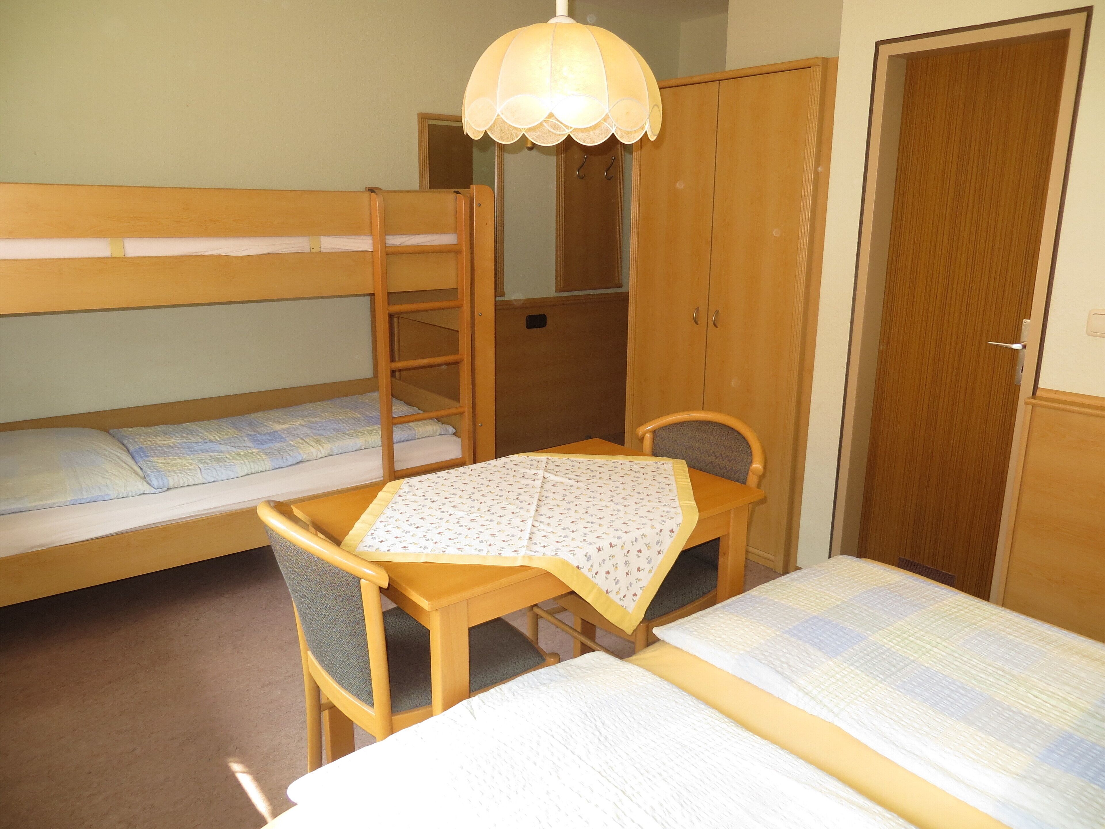 A dormitory room with bunk beds, a desk, a chair, and a wardrobe.