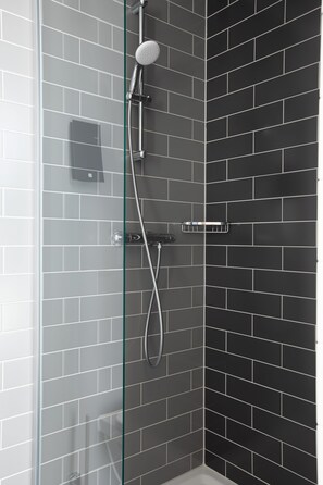 A shower with a glass door, a handheld showerhead, and a wall-mounted control panel.