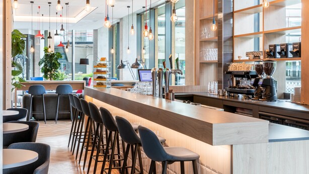 A modern bar area with a long counter, bar stools, and a coffee machine. - Holiday Inn Express Almere by IHG (Almere)