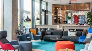 A modern lounge area with sofas, chairs, and tables, featuring large windows and pendant lighting. - Holiday Inn Express Almere by IHG (Almere)