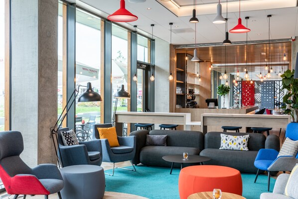 A modern lounge area with sofas, chairs, and tables, featuring large windows and pendant lighting.