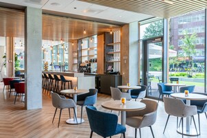 Un café moderno con mesas y sillas redondas, una zona de bar y grandes ventanales que dan a la calle.