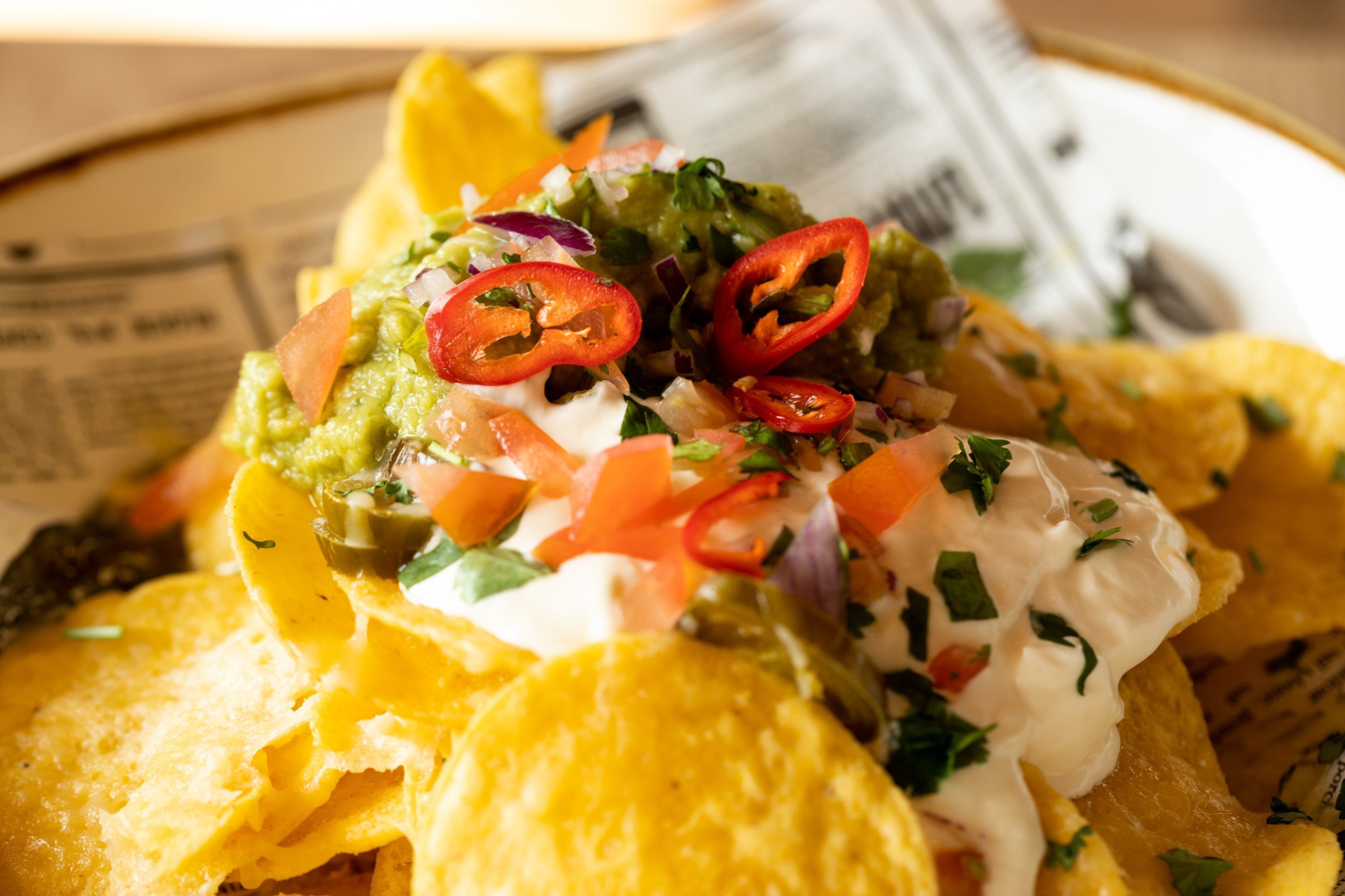 Nachos cubiertos de guacamole, crema agria, tomates picados y jalapeños en rodajas.