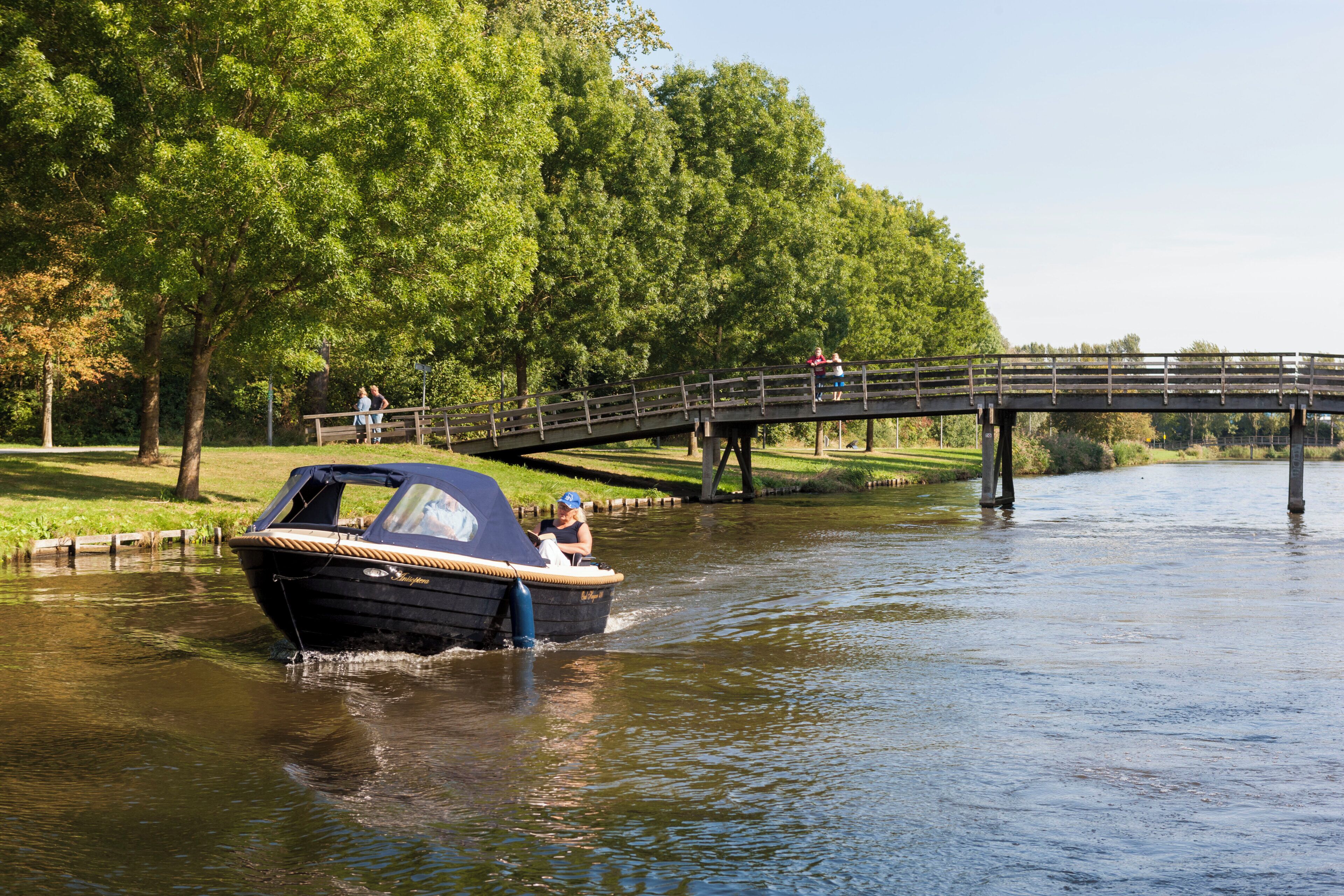 Een boot op een rivier, met een brug op de achtergrond.